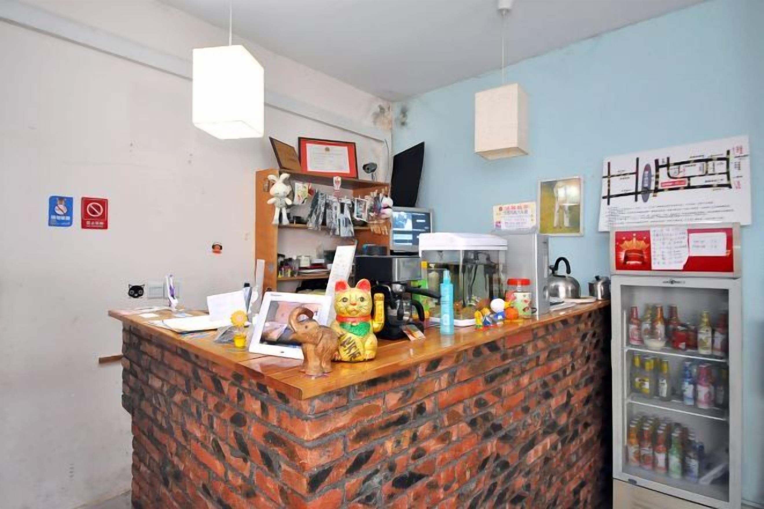 A reception desk with a brick counter, a computer, a refrigerator with beverages, and various items on the counter.