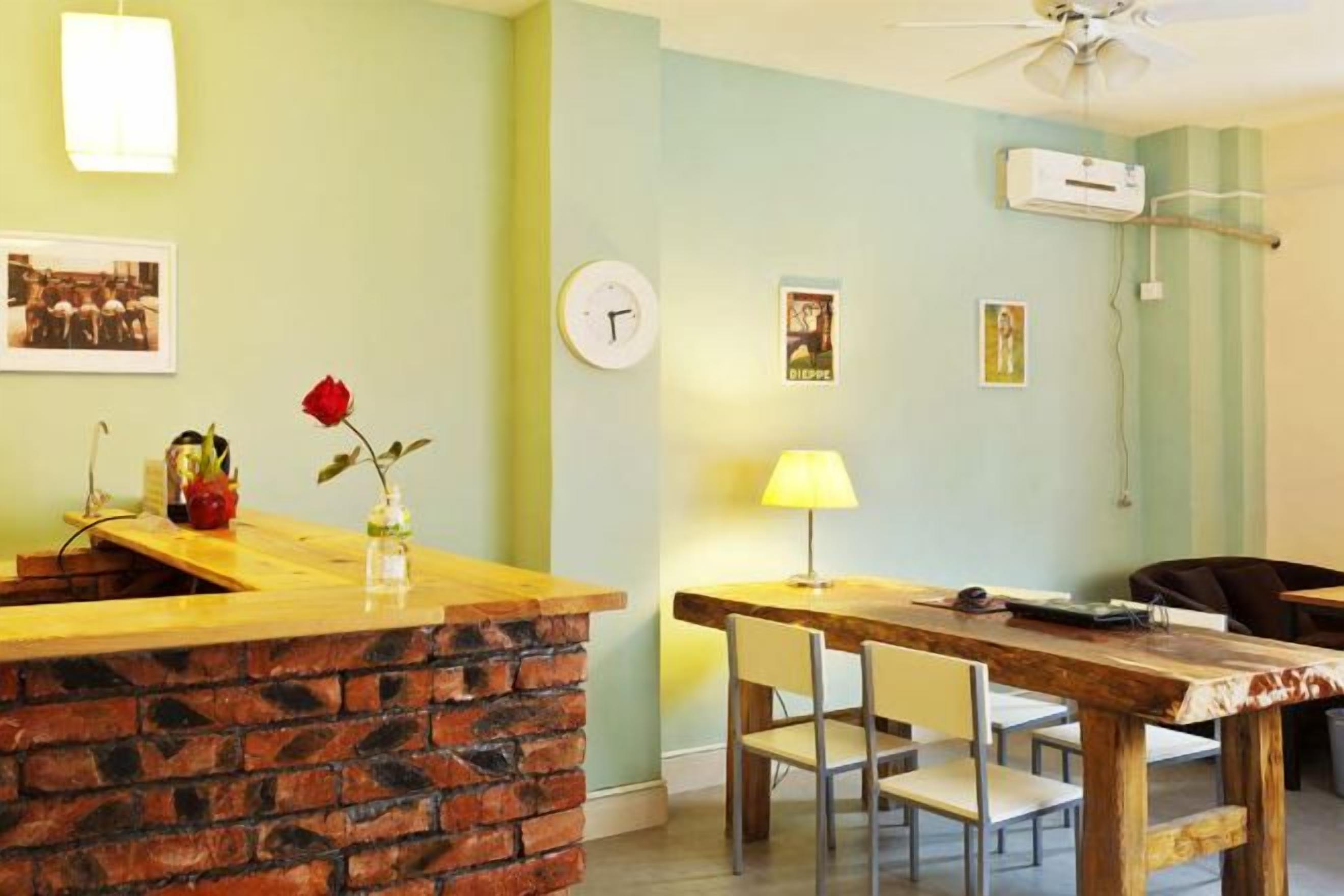 A room with a brick counter, a dining table with chairs, a clock, and wall-mounted air conditioning.