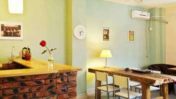 A room with a brick counter, a dining table with chairs, a clock, and wall-mounted air conditioning.