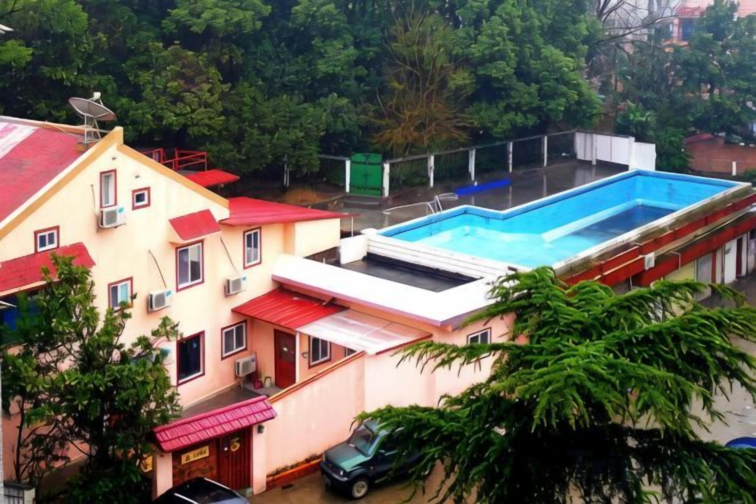 A residential building with a swimming pool, satellite dish, and a red-roofed structure.