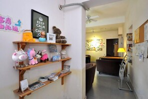 Un hall d’hôtel avec un comptoir d’accueil, une étagère fixée au mur où sont exposés des jouets en peluche et un panneau encadré.