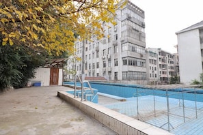A swimming pool with a wooden deck and a metal ladder, surrounded by a building with multiple balconies.