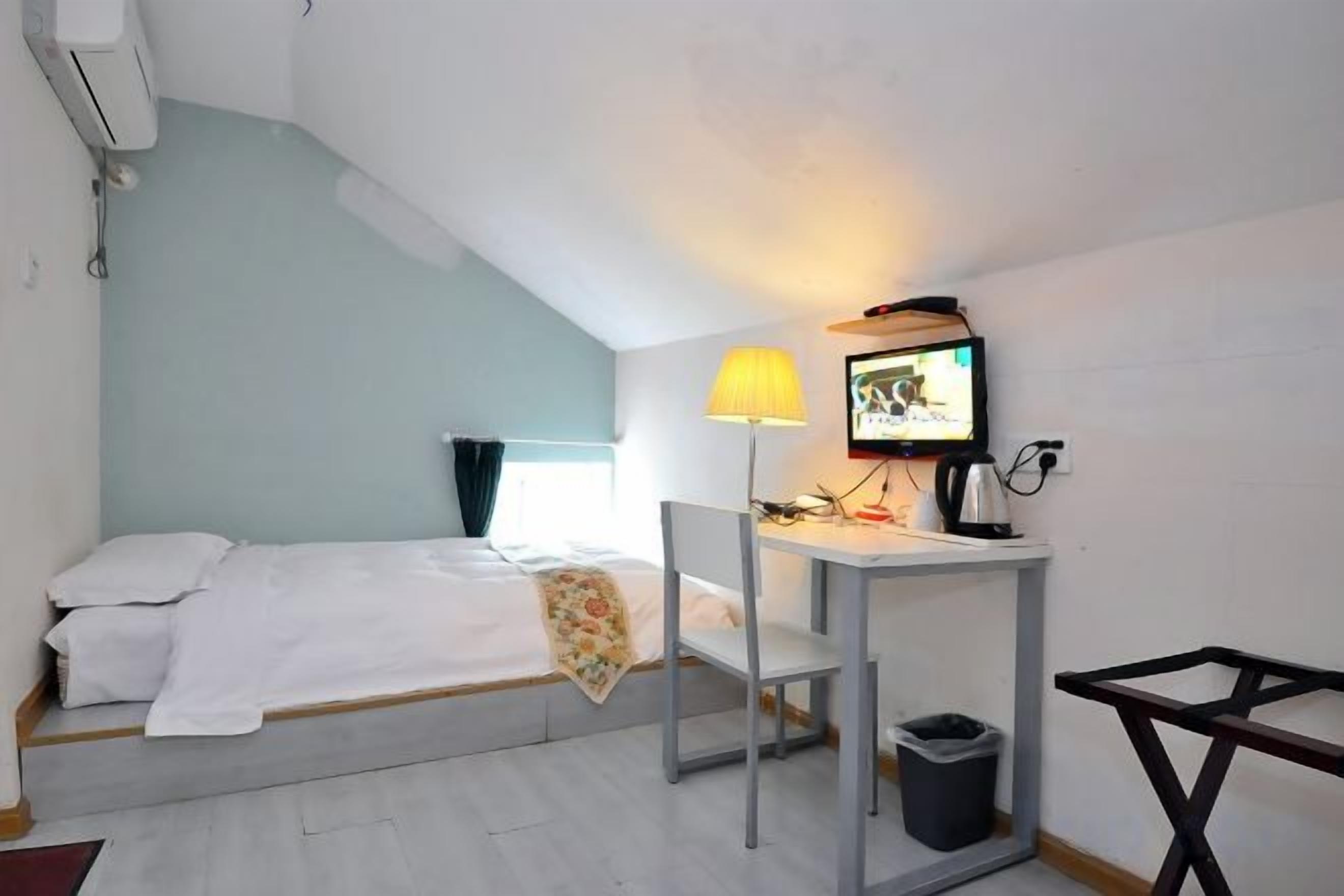 Habitación pequeña con una cama individual, escritorio, silla y televisor.