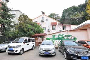 Un espace de stationnement avec plusieurs voitures, un bâtiment doté d’une antenne parabolique et une fresque représentant des fleurs.