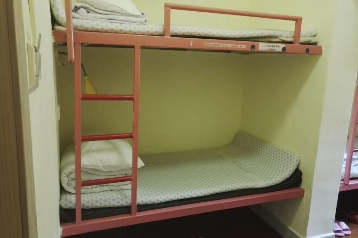 A bunk bed with a red frame, a mattress, and folded blankets.