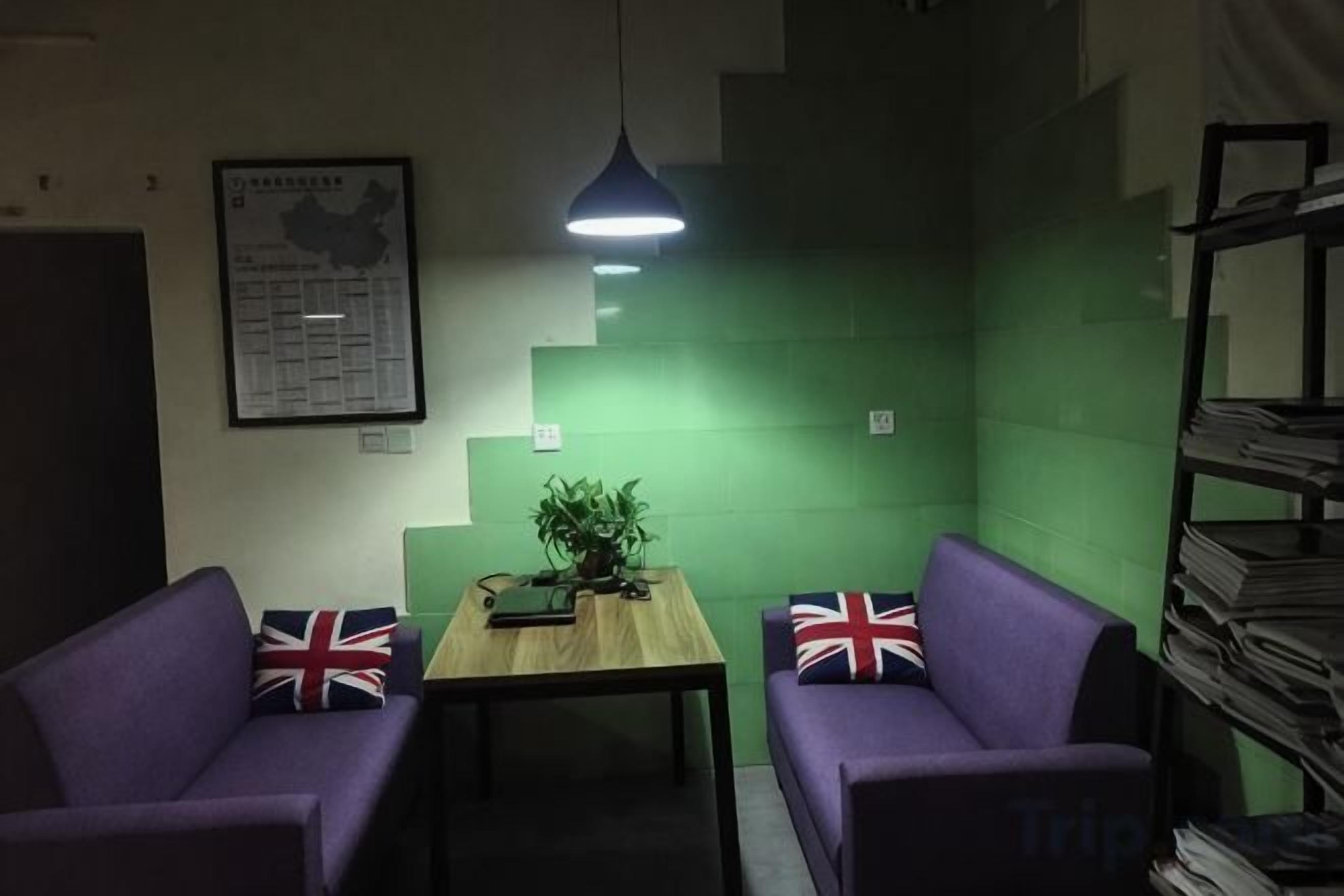 Una habitación con dos sofás morados, una mesa de madera, una pared verde, un mapa en la pared y una estantería con libros.