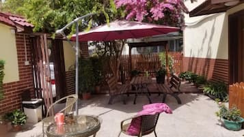 Un patio exterior con una mesa y sillas, rodeado de plantas en macetas y una valla de madera.