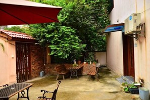 Een terras met een tafel en stoelen, een rode parasol en een bakstenen muur.
