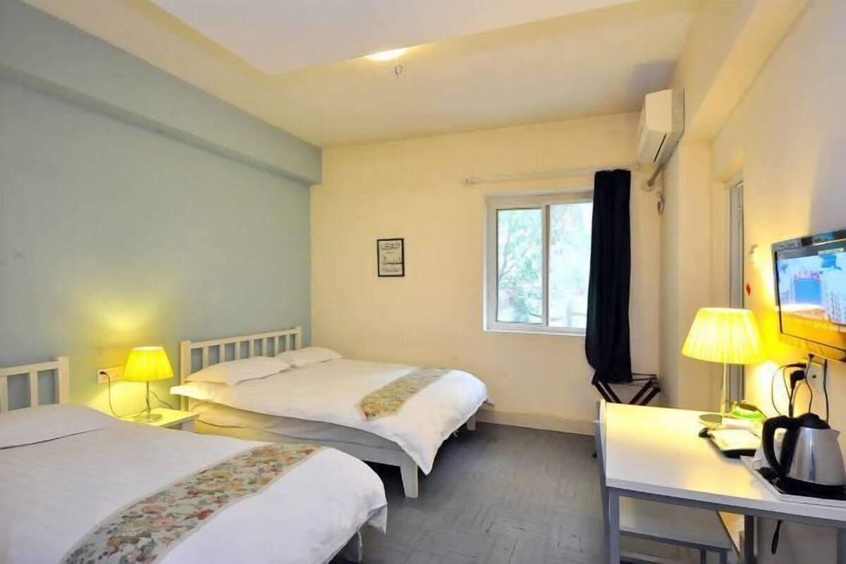 Une chambre d’hôtel avec deux lits, une télévision, un bureau avec une bouilloire et une fenêtre.
