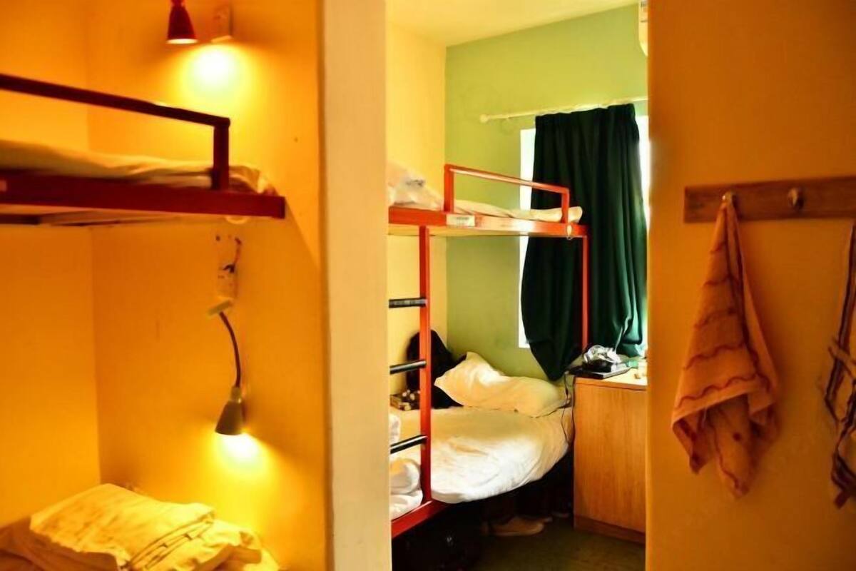 Une chambre de dortoir avec des lits superposés, un bureau et une fenêtre avec des rideaux.