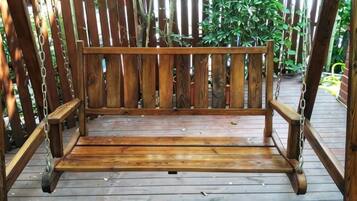 A wooden bench with a metal chain for hanging, set on a wooden deck with a wooden fence in the background.