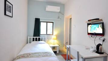 A bedroom with a bed, a desk, a television, and an air conditioning unit.