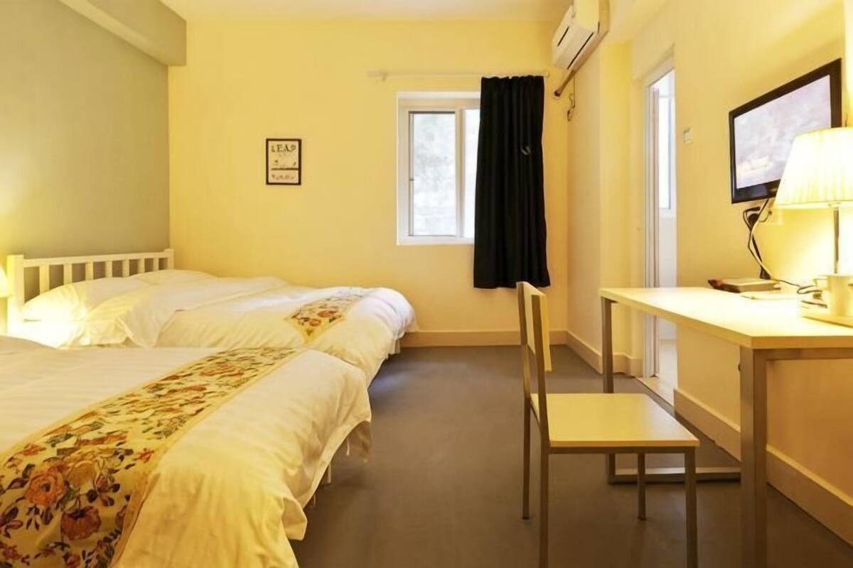 Une chambre d’hôtel avec deux lits, un bureau, une chaise, une télévision et une fenêtre avec des rideaux.