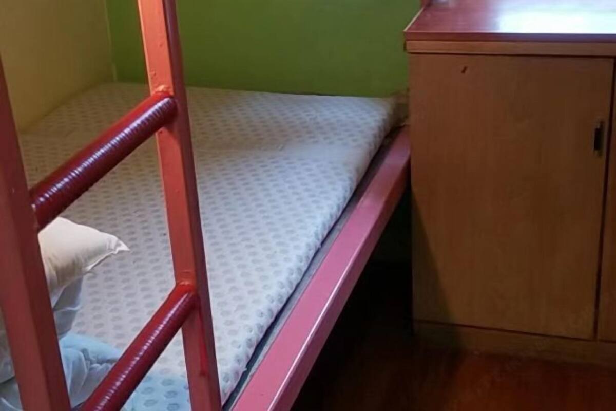Un lit superposé avec une structure rouge, une armoire en bois et un mur vert.