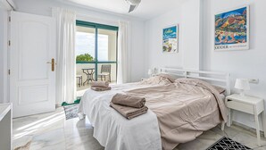 Un dormitorio con cama, mesita de noche, ventana con cortinas, ventilador de techo y vistas al exterior.