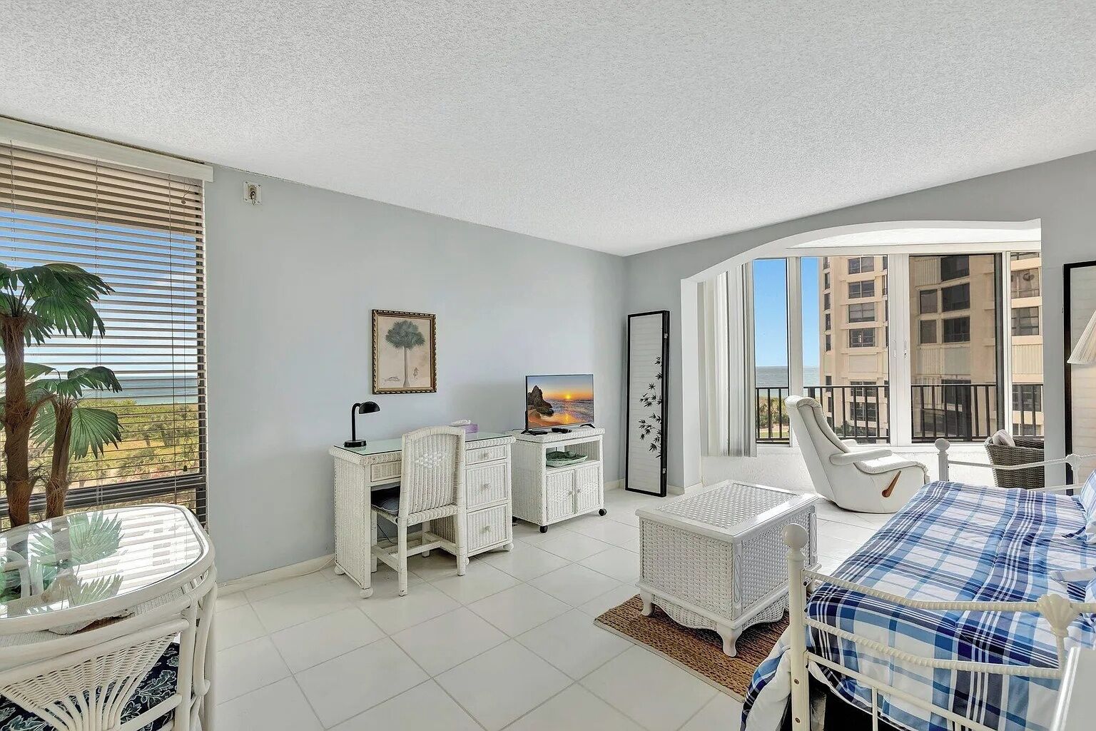 A bedroom with a bed, a desk, a chair, a TV, and a balcony with a view of the city.