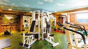 A gym with various exercise machines, a wall mural, and a view of the outdoors.