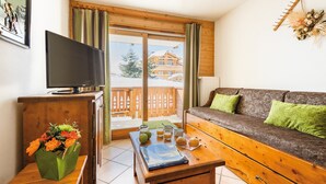 A cozy room with a wooden sofa, a TV on a wooden cabinet, a table with a book and glasses, and a view of a snowy mountain.
