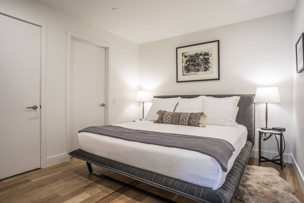 A bedroom with a bed, bedside lamps, a door, and a framed picture on the wall.