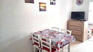 Uma sala de jantar com uma mesa posta para quatro pessoas, uma televisão sobre um móvel de madeira e três quadros na parede.
