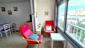 Uma varanda com mesa branca e duas cadeiras, uma mesinha com um vaso de flores e um enfeite fixado na parede.