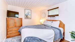 A bedroom with a bed, a wooden wardrobe, a painting, a lamp, and a window with blinds.
