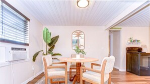 A dining area with a round wooden table and four chairs, a large plant, and a window with blinds.