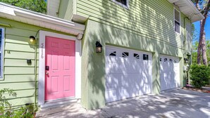 A two-story house with a green exterior, a pink front door, and two white garage doors.