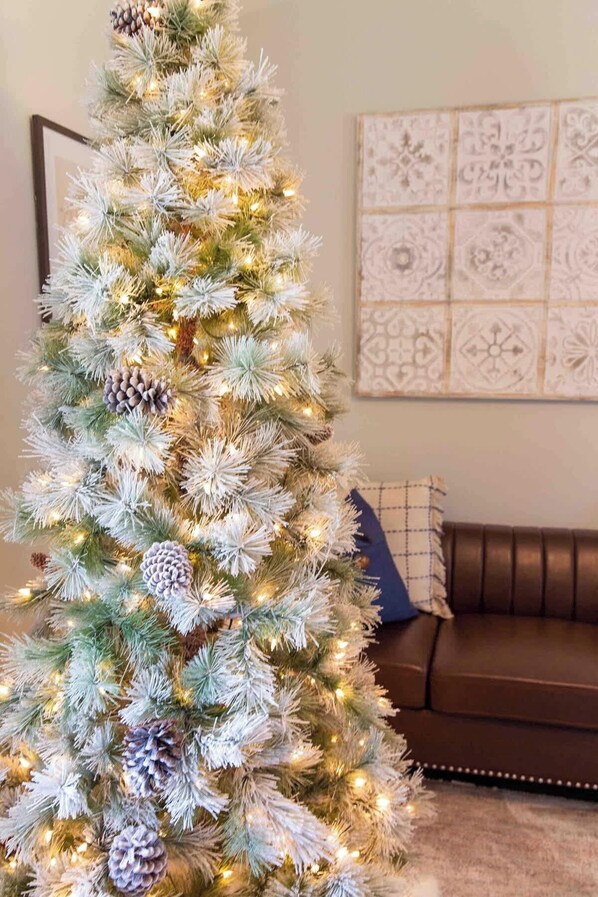 A Christmas tree with lights and pine cones, a brown leather couch, and a patterned wall in the background.