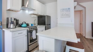 Una cuina compacta amb armaris blancs, una placa de cocció, un frigorífic i un rentaplat.
