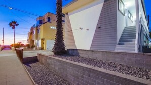 A modern building with a unique architectural design, featuring a combination of beige and white exterior walls, a visible staircase, and a landscaped area with gravel and a palm tree.