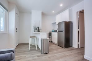 Kitchen features a compact island with sink and bar stools, stainless steel refrigerator, and a window.