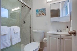 Une salle de bain avec une douche à parois de verre, des toilettes, un lavabo avec un miroir au-dessus et un tableau accroché au mur.