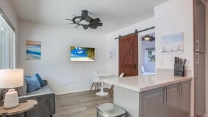 Et moderne køkken med en granitbordplade, lysegrå skabe og en indbygget ovn. Der er et hvidt spiseområde med et rundt bord og en sofa.