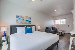 Una habitación de hotel moderna con una cama grande, un sofá, una mesita y un cuadro en la pared.