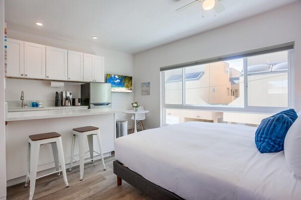 Una habitación de hotel moderna con una cama grande, una kitchenette pequeña, un área de comedor y vistas a la ciudad.