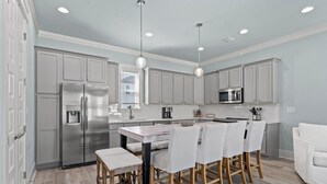 Una cocina moderna con armarios grises, electrodomésticos de acero inoxidable y una isla central con sillas.