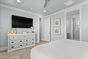 Une chambre à coucher avec un grand lit, une commode à tiroirs, un téléviseur à écran plat et des tableaux encadrés accrochés au mur.