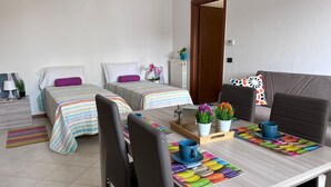 Een hotelkamer met twee bedden, een eettafel met stoelen en een bank. Er staan potplanten op de tafel.