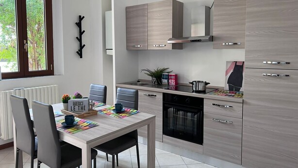 Een moderne keuken met lichte houten kastjes, een inbouwoven en een eethoek met een gedekte tafel voor twee personen.