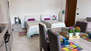 Hotelkamer met twee bedden, een eettafel met stoelen, een kitchenette en een badkamer die door een open deur zichtbaar is.