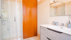 A bathroom with a wooden door, a shower, a sink with a mirror, and toiletries.