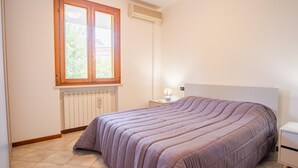 A bedroom with a bed, a window, a radiator, and a bedside table with a lamp.