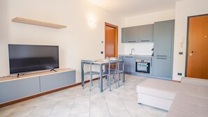 A compact living space with a TV, dining table, chairs, kitchenette, and a sofa.