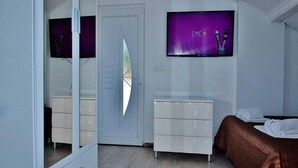 A modern hotel room with a large mirror, a flat-screen TV mounted on the wall, a bedside table with a brown bedspread, and a white dresser. - Apartments Brzica (Novi Vinodolski)