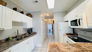 A narrow kitchen with white cabinets, a granite countertop, a microwave, and a stove. - First floor gorgeous condo in Myrtle Beach (Myrtle Beach)