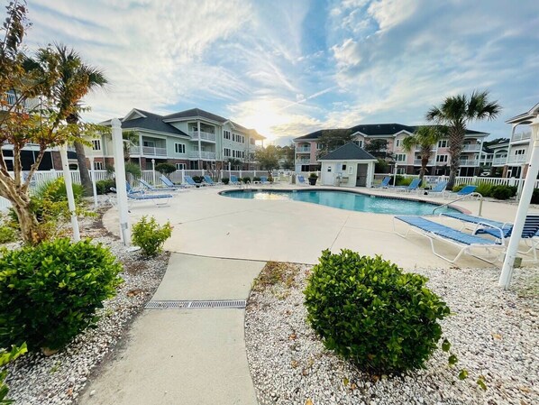 A pool area with lounge chairs, a small pool, and a pathway leading to a building with multiple balconies.