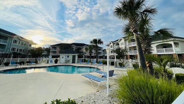 A swimming pool surrounded by lounge chairs and palm trees, with multi-story buildings in the background. - First floor gorgeous condo in Myrtle Beach (Myrtle Beach)
