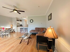 A modern living room with a dining area, a kitchen in the background, and a ceiling fan.