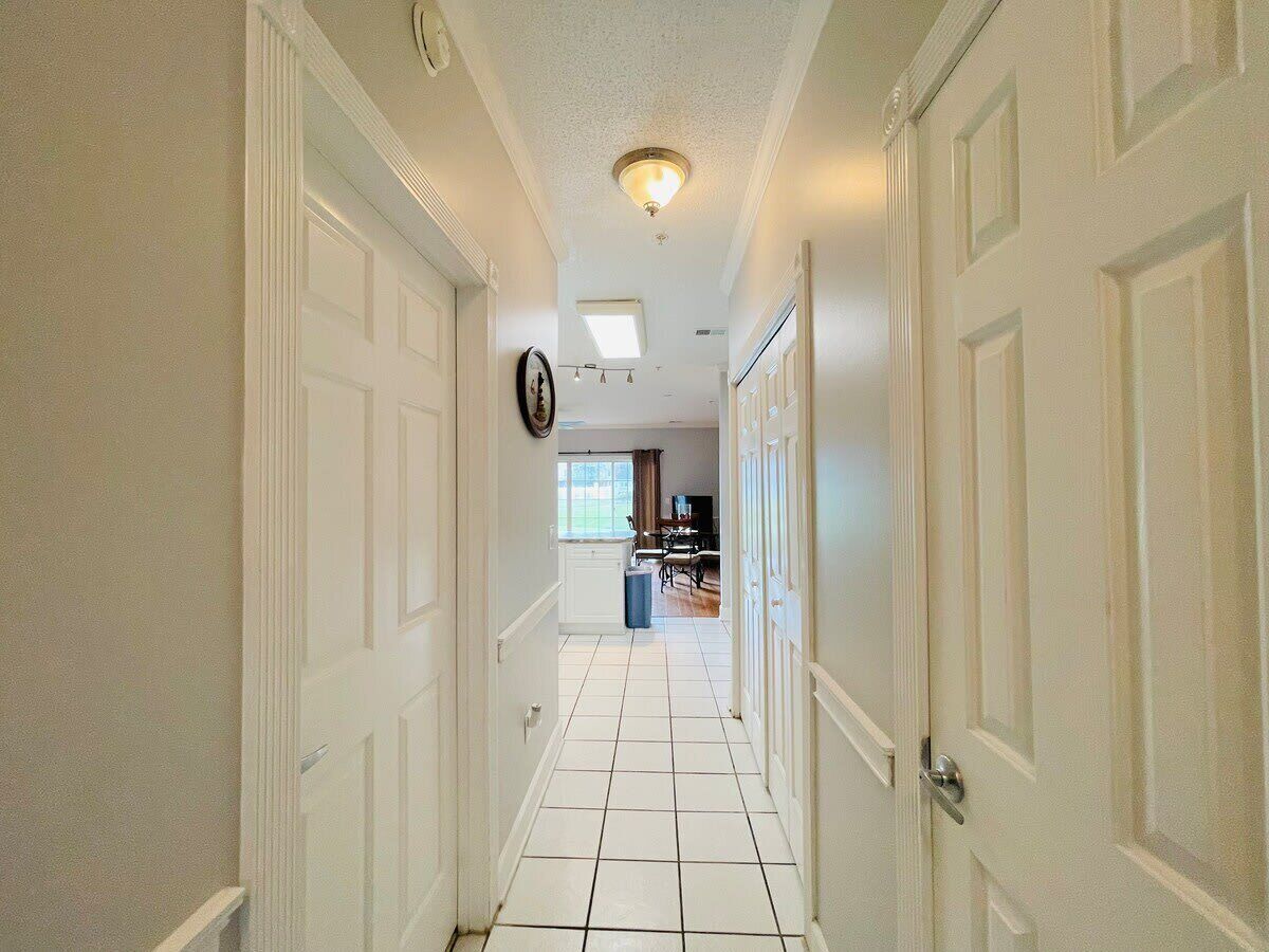 Corredor com portas brancas, um relógio na parede e vista para uma sala de jantar com mesa e cadeiras.